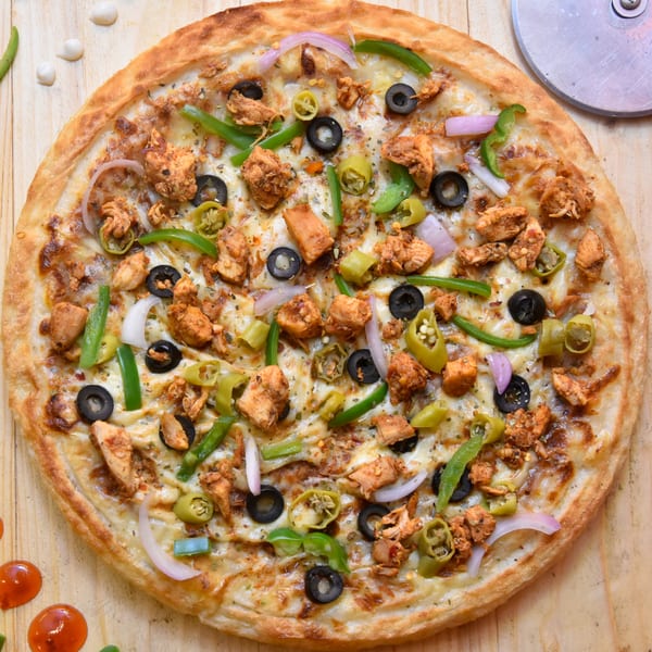 Tommy's Pizza with chicken, olives, green peppers, and onions on a wooden surface.