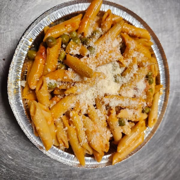 Penne pasta with tomato sauce, green peas, and grated cheese in a foil takeout container.