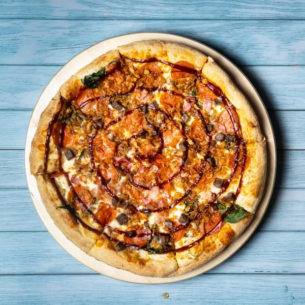 Tommy's Pizza with pepperoni, ham, beef, crispy onions, and BBQ sauce drizzle on a blue wooden table.