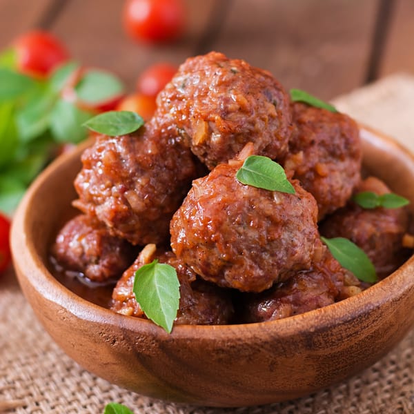 Tommy's Pizza and Pasta meatballs in a wooden bowl, garnished with fresh basil and cherry tomatoes.